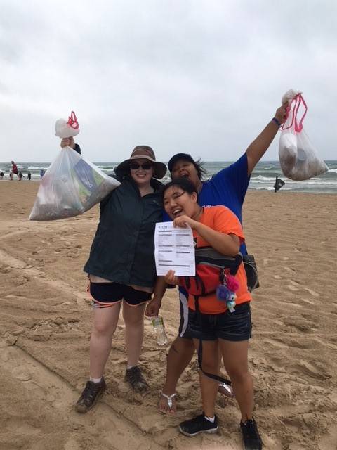 3 students showing the trash they have picked up and their tracking sheet